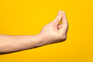 Close-up of a stout man's hand making the Italian gesture of ma que cosa face, isolated on yellow background.