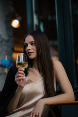 A girl in a light dress and a jacket. A girl with a glass of cocktail in her hands. A girl drinks white wine. A charming stranger. Vertical stock photo