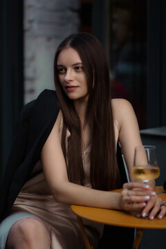 A girl in a light dress and a jacket. A girl with a glass of cocktail in her hands. A girl drinks white wine. A charming stranger. Vertical stock photo