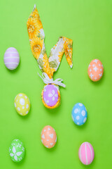 Happy Easter holiday greeting card design concept. Colorful Easter Eggs and spring flowers on pastel green background. Flat lay, top view, copy space.