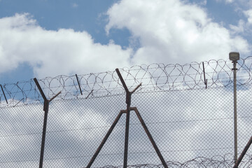 High wire fence with barbed wire against blue sky background. Border, protection zone