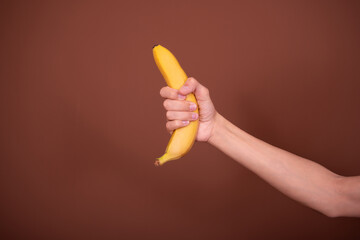 Fototapeta na wymiar A man's hand is holding a yellow banana. Brown background.