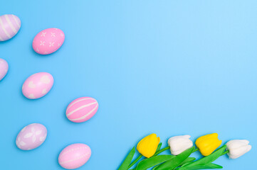 Happy Easter holiday greeting card design concept. Colorful Easter Eggs and spring flowers on blue background. Flat lay, top view, copy space.