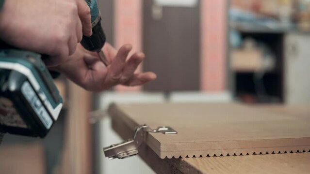 Man assembling furniture. A worker is screwing a hinge into a wooden cabinet door with a screwdriver, close-up. 