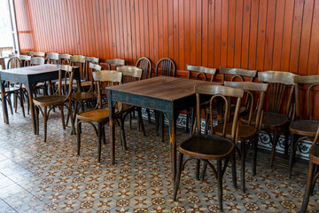 Selective focus on antique brown wooden chairs with vintage style in front of red brown wooden wall covering background. Traditional Thonet chairs on authentic karo cement tiles in the cofee shop. 