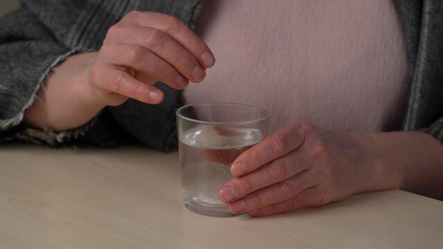 a woman takes medicine - an instant tablet A woman throws an effervescent soluble tablet into a glass of water at home