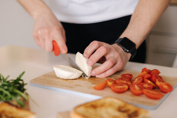 Obraz na płótnie Canvas Man slice peace of mozzarella on wooden board. Preparing Italian classic sandwich