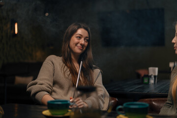 Beautiful young woman inhaling hookah girl smoking hookah sitting in lounge bar concept of...