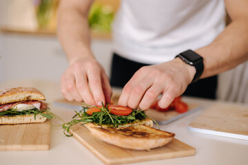Obraz na płótnie Canvas Young man put tomatoes on sandwich. Man preparing lunch at home