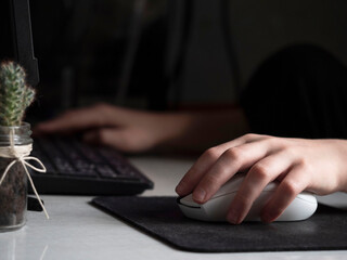 A teenager's hand holding a white computer mouse. Close-up. A teenager sits at his desk and plays computer games.