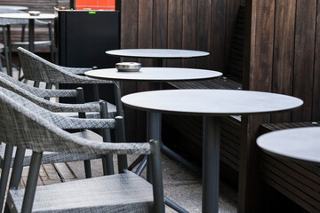 Ashtray on table for smoking outdoors. Empty tables and chairs outside restaurant or cafe or bar. 