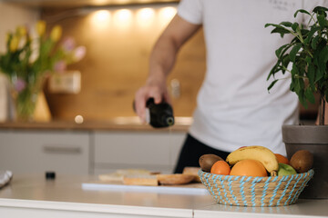 Obraz na płótnie Canvas Close-up of man spreads olive oil on baguette. Bright kitchen interior. Focus on basket of fruits