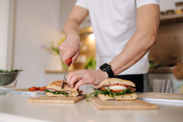 Obraz na płótnie Canvas Middle selection of man blogger slice Italian sandwich in the kitchen. Close-up of bruschetta in hands