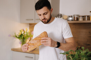 Handsome bearded man smell a freshly baked baguette. Home food concept 