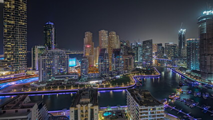 Obraz premium Panorama showing Dubai Marina with several boat and yachts parked in harbor and skyscrapers around canal aerial night timelapse.