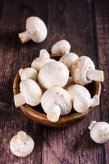 Whole fresh champignons in a plate and on a wooden table vertical view