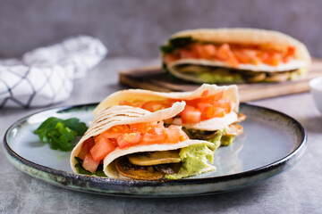 Tortilla with guacamole, fried mushrooms, tomatoes and herbs on a plate