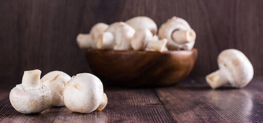 Close-up whole fresh champignons on a wooden table and in a bowl on the background web banner