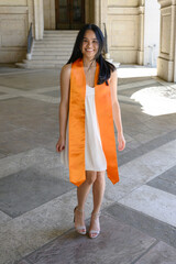 Young attractive Asian American college student, wearing gown and sash, celebrating her graduation from the university