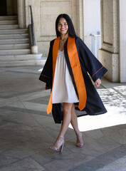 Young attractive Asian American college student, wearing gown and sash, celebrating her graduation...