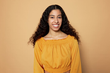 Studio shot of young pretty latin girl with long dark hair looking at camera with candid smile. Student girl happy with beginning of summer vacations, standing against brown background