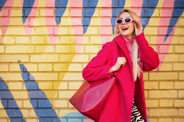 Fashionable happy smiling blonde woman wearing trendy pink sunglasses, fuchsia color coat, with...