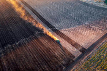 An industrial tractor plows the ground field from a bird's eye view.