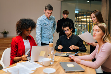 Fototapeta premium Portrait of multiethnic male and female colleagues working with project documents at meeting in boardroom, sitting at table, analyzing statistics, reading financial report, discussing strategy.