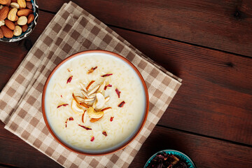 Rice pudding served in clay bowl. Indian rice kheer with nuts on a wooden background. Popular...