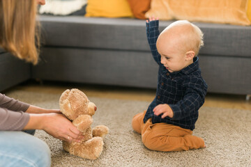 Happy toddler boy playing with her teddy bear at house - childhood and child development stages concept