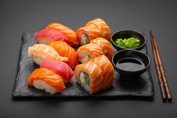 Set of traditional Japanese sushi and rolls angle view with soy sauce and wasabi on dark black rustic slate. Sushi with salmon, tuna and shrimp