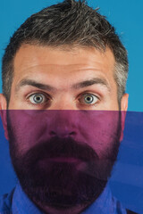 Color concept. Bearded man hiding her face behind colored glass. Serious bearded man partially closed by glass. Vivid colors. Closeup portrait. Fashion man in denim shirt with acolored items.