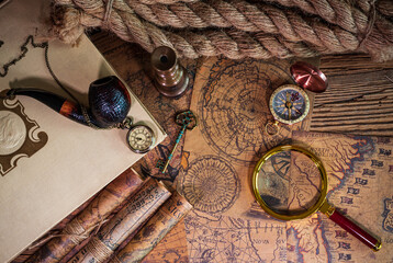 Old objects, book, magnifying glass, compass, pocket watch, spyglass, thick rope, tobacco pipe, old key lying on old maps in flat lay view