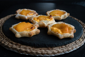 Puff pastry with custard, peach on round black slate, moody dark pictures with shallow depth of field.