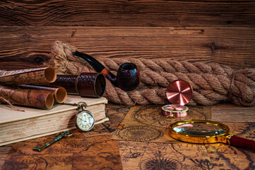 Old objects, book, magnifying glass, compass, pocket watch, spyglass, thick rope, tobacco pipe, old key lying on old maps
