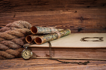 Old items, map scrolls and a pocket watch lying on an old book next to a thick rope