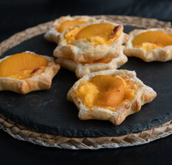 Puff pastry with custard, peach on round black slate, moody dark pictures with shallow depth of field.