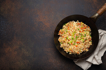 Authentic Chinese and Asian fried rice with egg and vegetables in wok top view on rustic concrete...