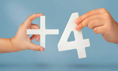 The number four and the plus symbol in the hands of a child on a blue background. White number 4 plus close up. Add three concept.