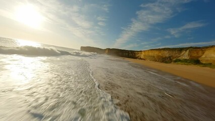 A drone flies along the ocean with waves at sunset next to a rock in Australia - Powered by Adobe
