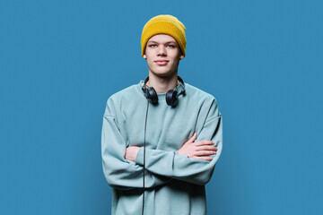 Young male in yellow cap sweatshirt with headphones on blue background