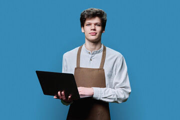 Young male in an apron with laptop, on blue background