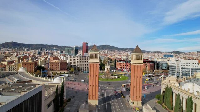 Panoramic aerial drone view of city traffic Plaza de Espana of Squares in Barcelona with Venetian Towers and Arenas de Barcelona. Cars driving around monumental fountain of Placa de Espanya. 4K video