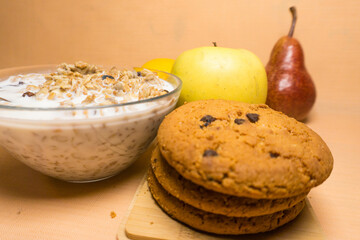muesli in a glass bowl with milk, red pear, yellow apple, lemon, oatmeal cookies with chocolate