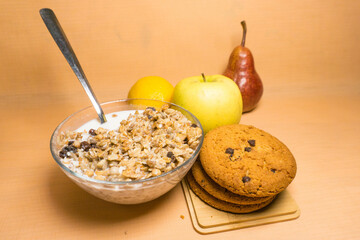 muesli in a glass bowl with milk, red pear, yellow apple, lemon, oatmeal cookies with chocolate