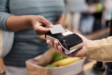 Close up of unrecognizable black woman paying via credit card in supermarket and buying groceries, copy space