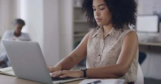 Young business woman typing on a laptop while sitting at a desk in her office. Creative professional with an afro typing an email and smiling at her job. Confident woman focused on sending an email