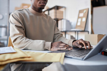Fototapeta na wymiar Close-up of young male manager of storage room typing on laptop keyboard while sitting by workplace and checking new online orders