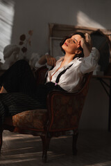 Obraz premium beautiful brunette woman in an armchair in the rays of the sun from the window.