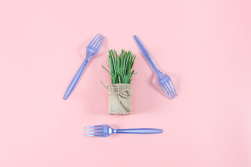 Three blue plastic forks arranged in a triangle with a flower in a burlap pot on a pink background